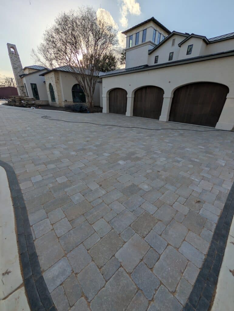 6500 sq ft paver driveway installation in San Antonio featuring Unilock Brussels Block 3-piece pattern with dark charcoal Mattoni border in front of custom home
