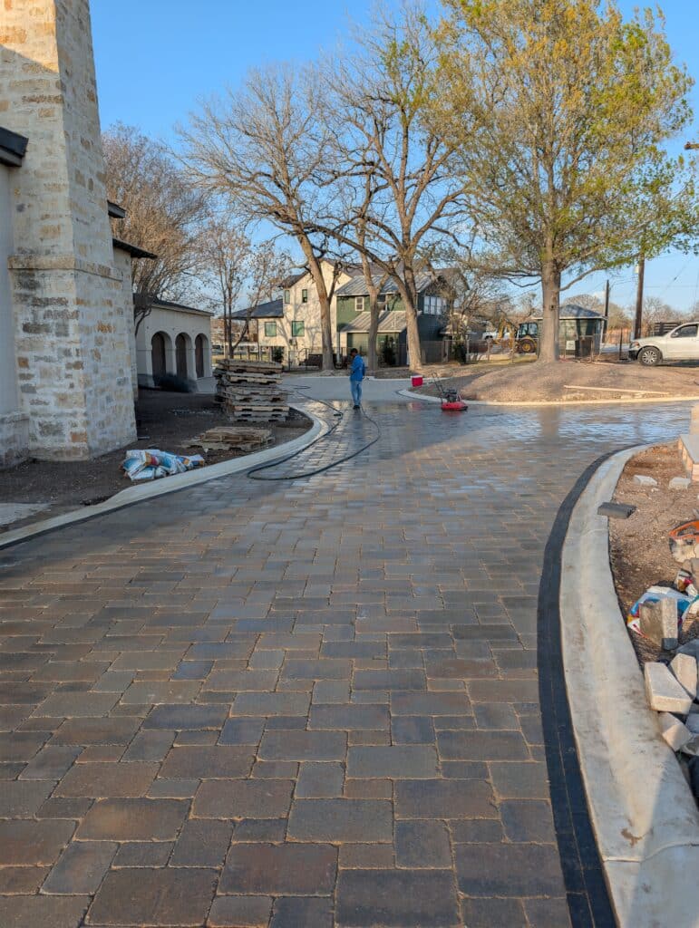 Freshly cleaned and sealed paver driveway showing Unilock Brussels Block 3-piece pattern with dark charcoal Mattoni border, 6500 sq ft driveway project