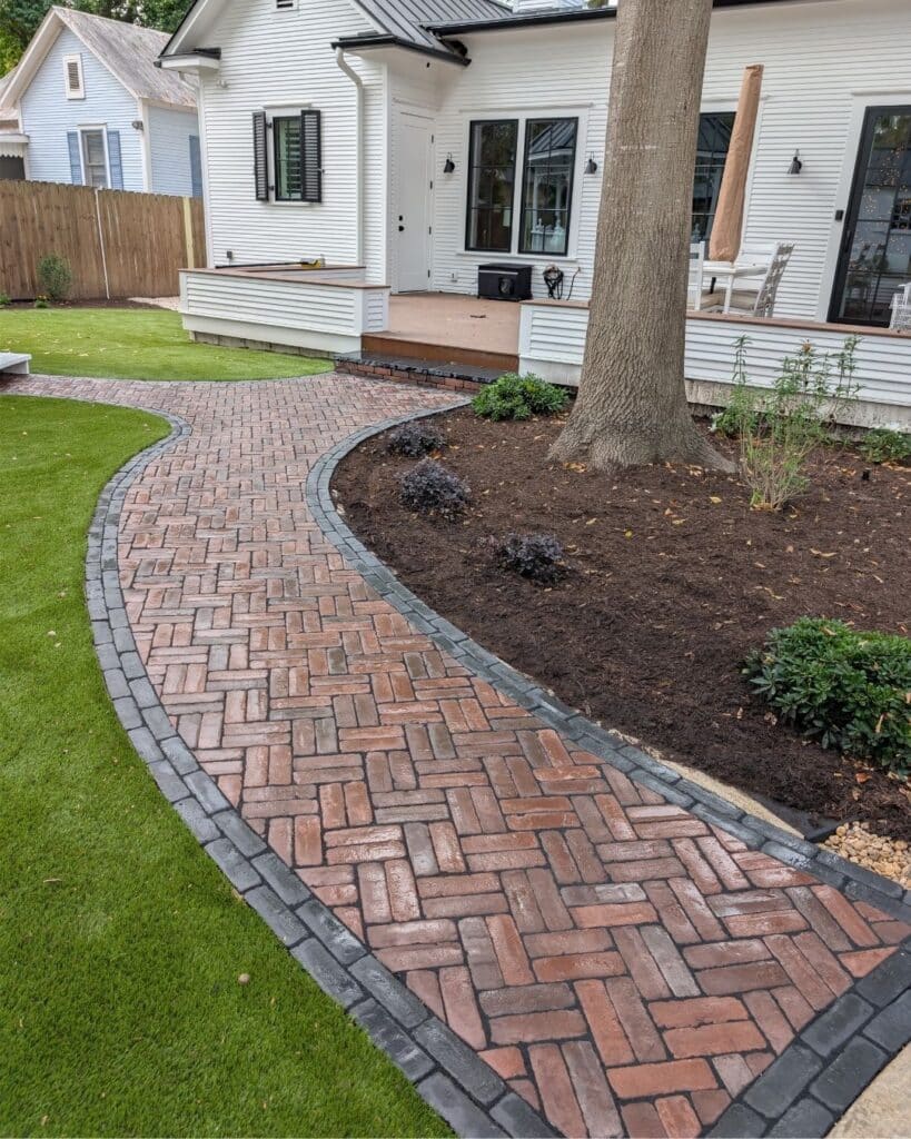 Elegant curved backyard path featuring a double herringbone paver pattern and black borders
