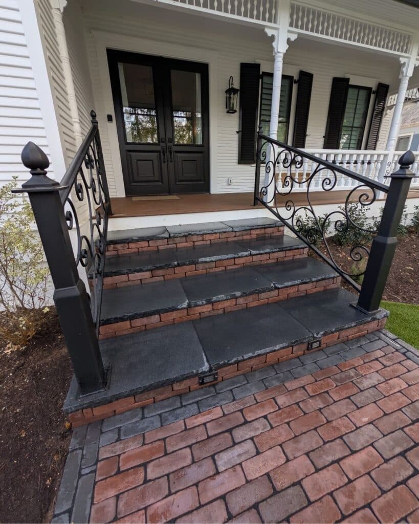Custom masonry entrance steps with dark natural limestone treads and vertical paver risers